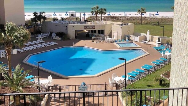 Zona de piscina con dos piscinas, sillas de descanso y vista a la playa.