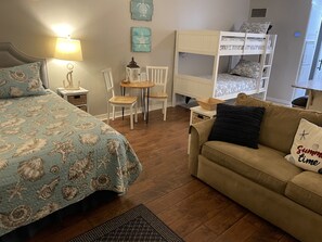 A bedroom with a bunk bed, a bed with a patterned bedspread, a small round table, two chairs, a sofa, and a lamp. - Beach Front Studio Direct Gulf View King and bunks (Panama City Beach)
