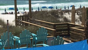 Una terraza frente al mar con barandas de madera, sillas Adirondack azules y sombrillas.