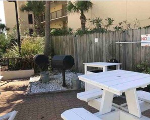 A patio area with a white table and benches, a grill, and a wooden fence. - Beach Front Studio Direct Gulf View King and bunks (Panama City Beach)