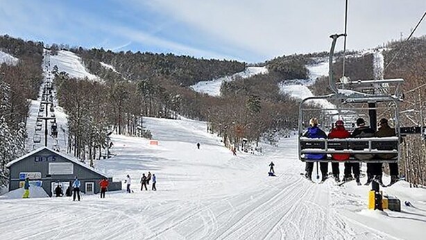 A ski lift with passengers, a snow-covered slope, and a lodge with a sign.