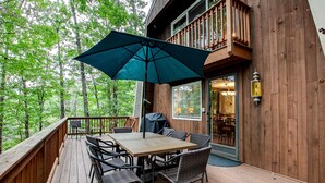 A wooden deck with a table and chairs, an umbrella, and a view of a forested area.