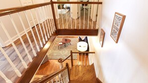 A wooden staircase with a white railing, leading to a room with a patterned rug, a small round table, and a chair. - Private Retreat w/Pool, Hot Tub & Fire Pit, Perfect for Groups! (Warwick)