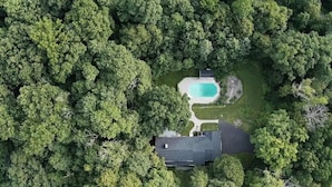 An aerial view of a property with a swimming pool surrounded by dense trees, a visible house, and a well-maintained lawn. - Private Retreat w/Pool, Hot Tub & Fire Pit, Perfect for Groups! (Warwick)