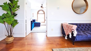 A room with a wooden floor, a blue sofa, a large mirror, and a potted plant. - Private Retreat w/Pool, Hot Tub & Fire Pit, Perfect for Groups! (Warwick)
