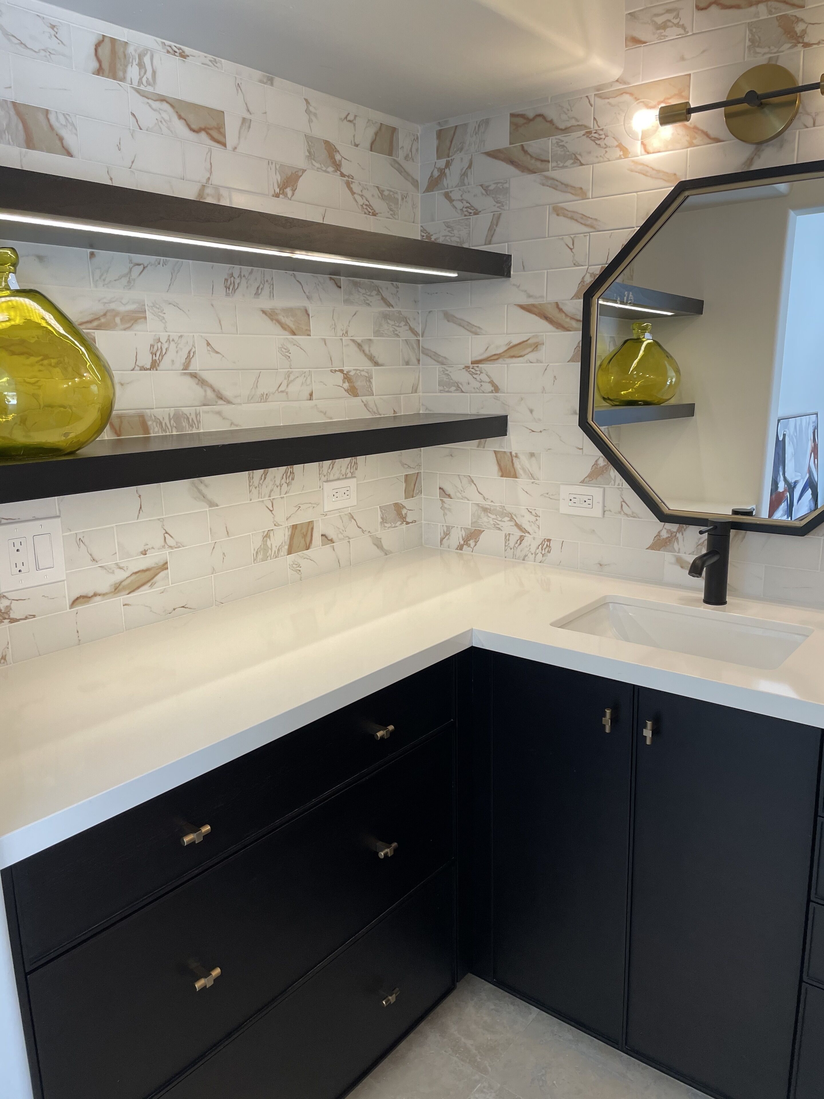 Casa de banho moderna com bancada branca, armários pretos e azulejos com padrão marmorizado.