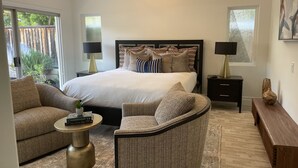 Een moderne slaapkamer met een groot bed, twee nachtkastjes, een bank, een stoel en een houten bankje.