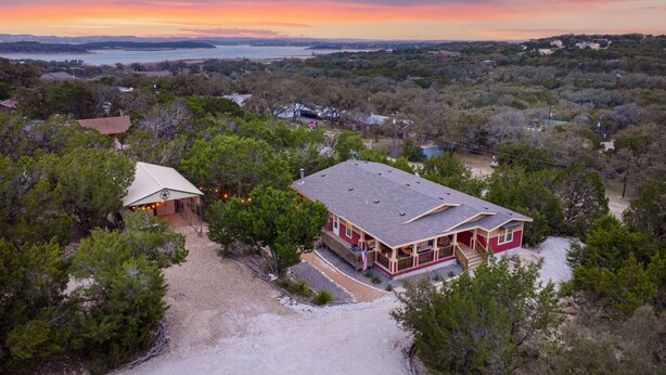 Una casa grande con una terraza amplia y un área cubierta, rodeada de árboles frondosos y vista al océano al atardecer.