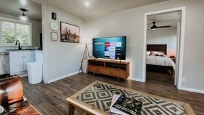 Ein modernes Wohnzimmer mit Fernseher, Couch, einem Couchtisch mit einem Buch sowie einer Küchenzeile mit Schränken und Spüle.