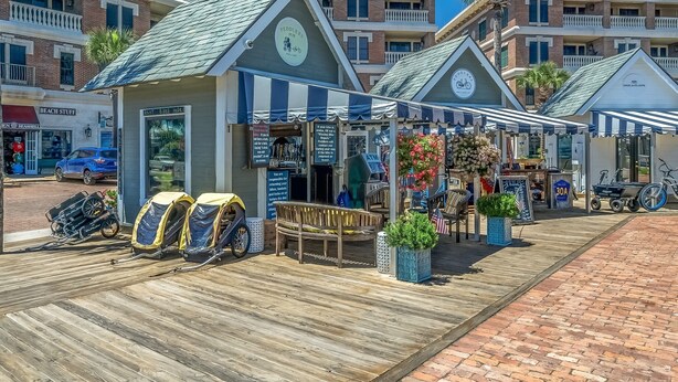 A beachfront boardwalk with a row of beachside shops, including a bike rental service and a café. - Village Of South Walton #263A | Luxe Condo in the Village! (Seacrest Beach)