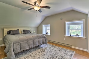 A bedroom with a bed, two windows, a ceiling fan, and a rug.