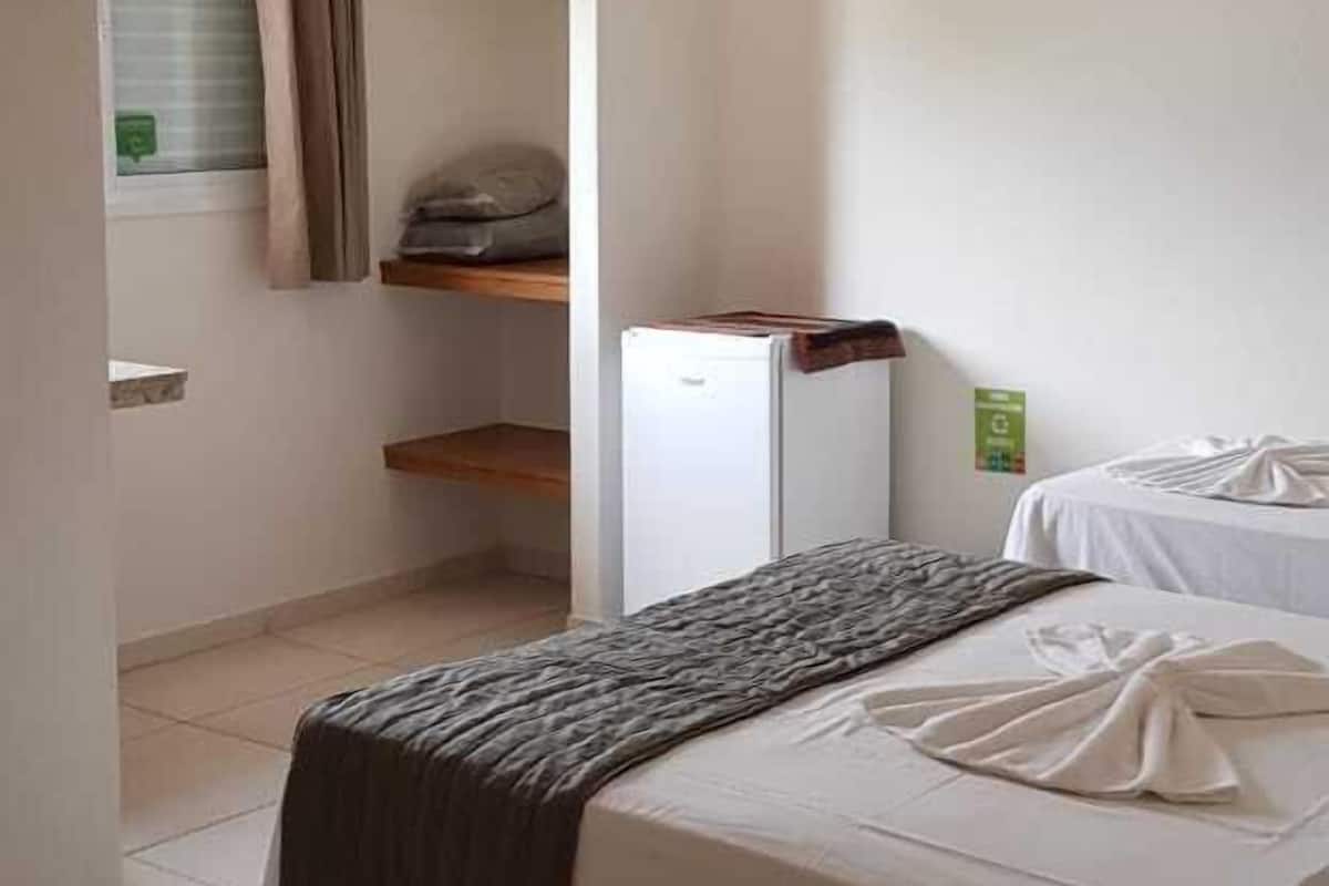 Un dormitorio con cama, armario, estante y ventana con cortinas.