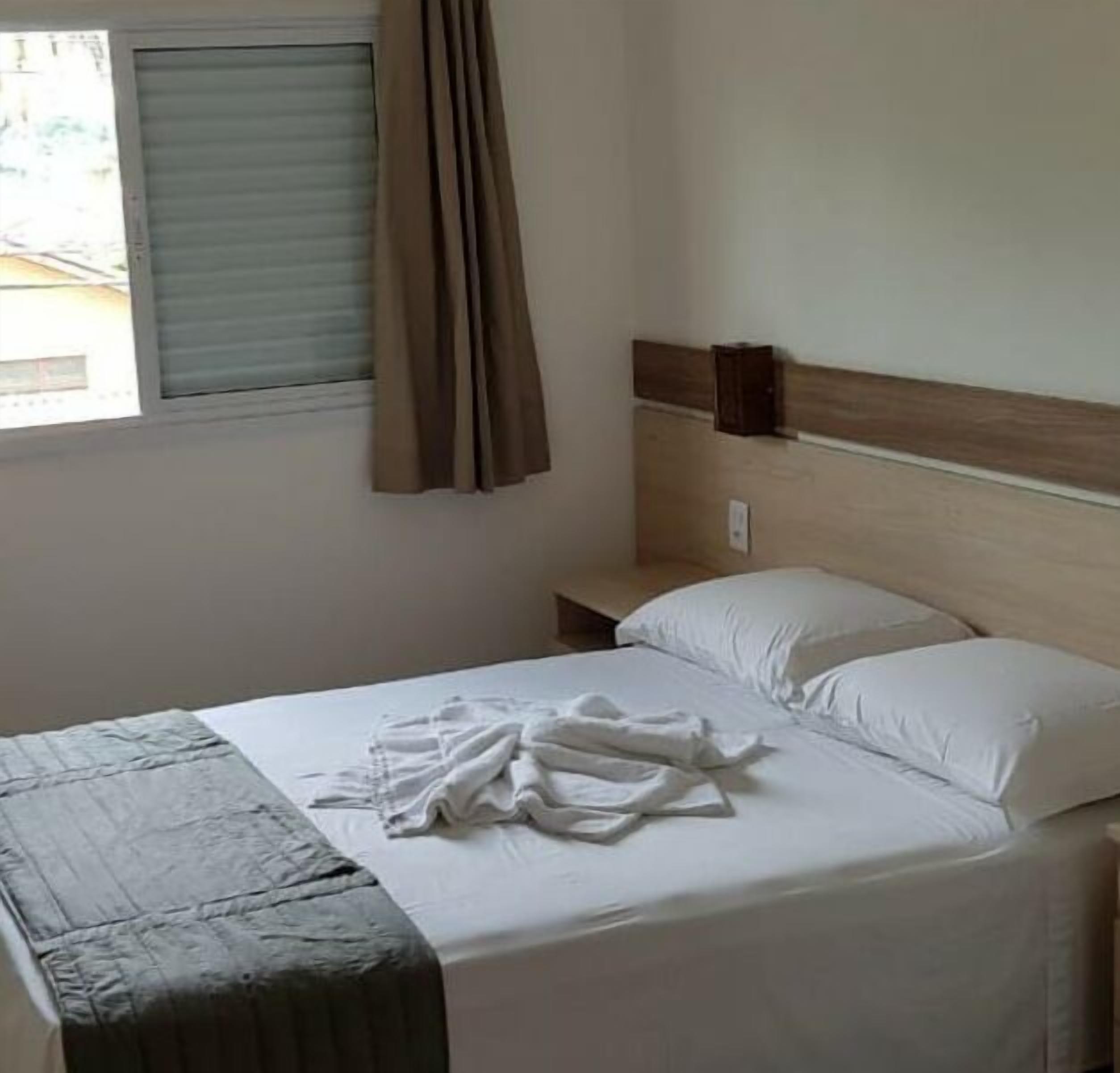 A hotel room with a bed, a nightstand, a window with curtains, and a wooden headboard.