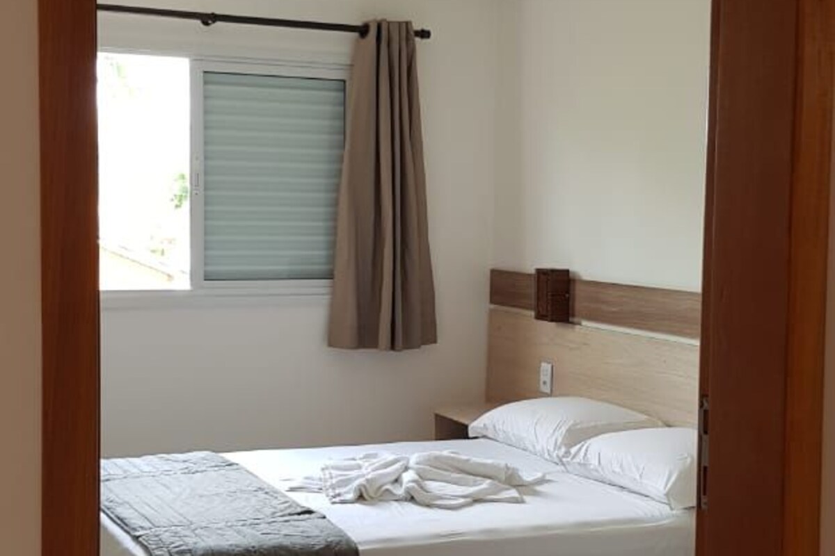 Een slaapkamer met een bed, een raam met gordijnen en een houten hoofdbord.