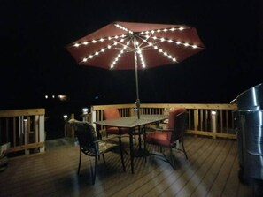 En uteplats med ett bord och stolar, ett parasoll med belysning och en grill.