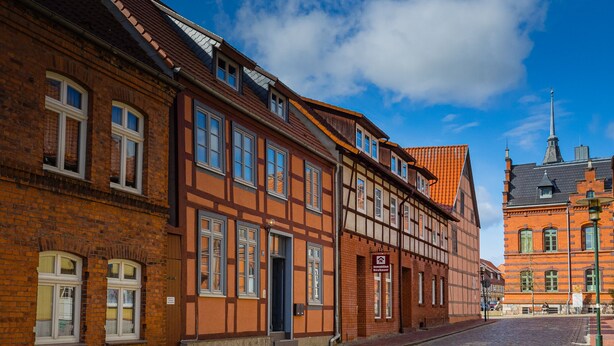 Une rue bordée de bâtiments traditionnels à colombages, une rue pavée et un ciel d’un bleu éclatant.