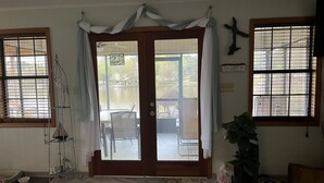 Ein Zimmer mit einer Schiebeglastür, die auf eine Terrasse mit Sitzmöbeln führt, einem Deckenventilator und Blick auf einen See.