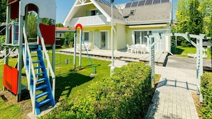 A playground with a slide and climbing structure, a house with solar panels, and a patio with outdoor furniture. - Wonderful private villa for 12 guests with private pool, A/C, WIFI, TV and terrace (Keszthely)