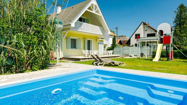 A swimming pool with lounge chairs, a yellow house with a white balcony, and a playground with a slide. - Wonderful private villa for 12 guests with private pool, A/C, WIFI, TV and terrace (Keszthely)