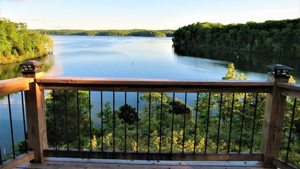 A wooden deck with a railing overlooking a calm lake surrounded by dense forest. - Tiny Home at Kentucky Lake's Lynnhurst Family Resort (Murray)