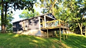 A two-story house with a wooden deck and a large tree in the background. - Tiny Home at Kentucky Lake's Lynnhurst Family Resort (Murray)