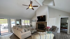 A spacious living room with a fireplace, a ceiling fan, and a large TV. - Little Buck Bungalow - Deerfield Lake View Home on Norris Lake (LaFollette)