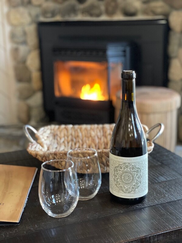 A bottle of wine, two glasses, and a woven basket on a table in front of a fireplace.
