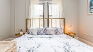 A bedroom with a bed, a nightstand, a lamp, and a window with sheer curtains. - Downtown Guild #3 | Mag Mile Gold Coast The Lake! (Chicago)