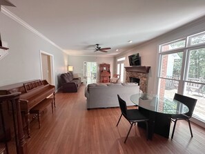 A spacious living room with a fireplace, a dining area with a glass table, and a large window offering a view of the outdoors.