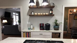 Una cocina con estufa a gas, cafetera y estantes con utensilios de cocina.