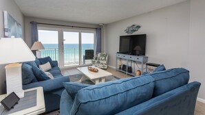 En stue med sofa, sofabord, TV og en balkon med havudsigt.