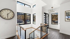 Un interior moderno con una escalera, ventanas amplias y un reloj en la pared.