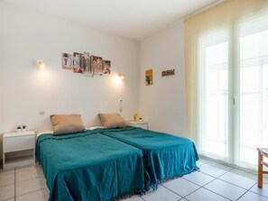 A bedroom with two beds, a nightstand, a small table, and a window with curtains.