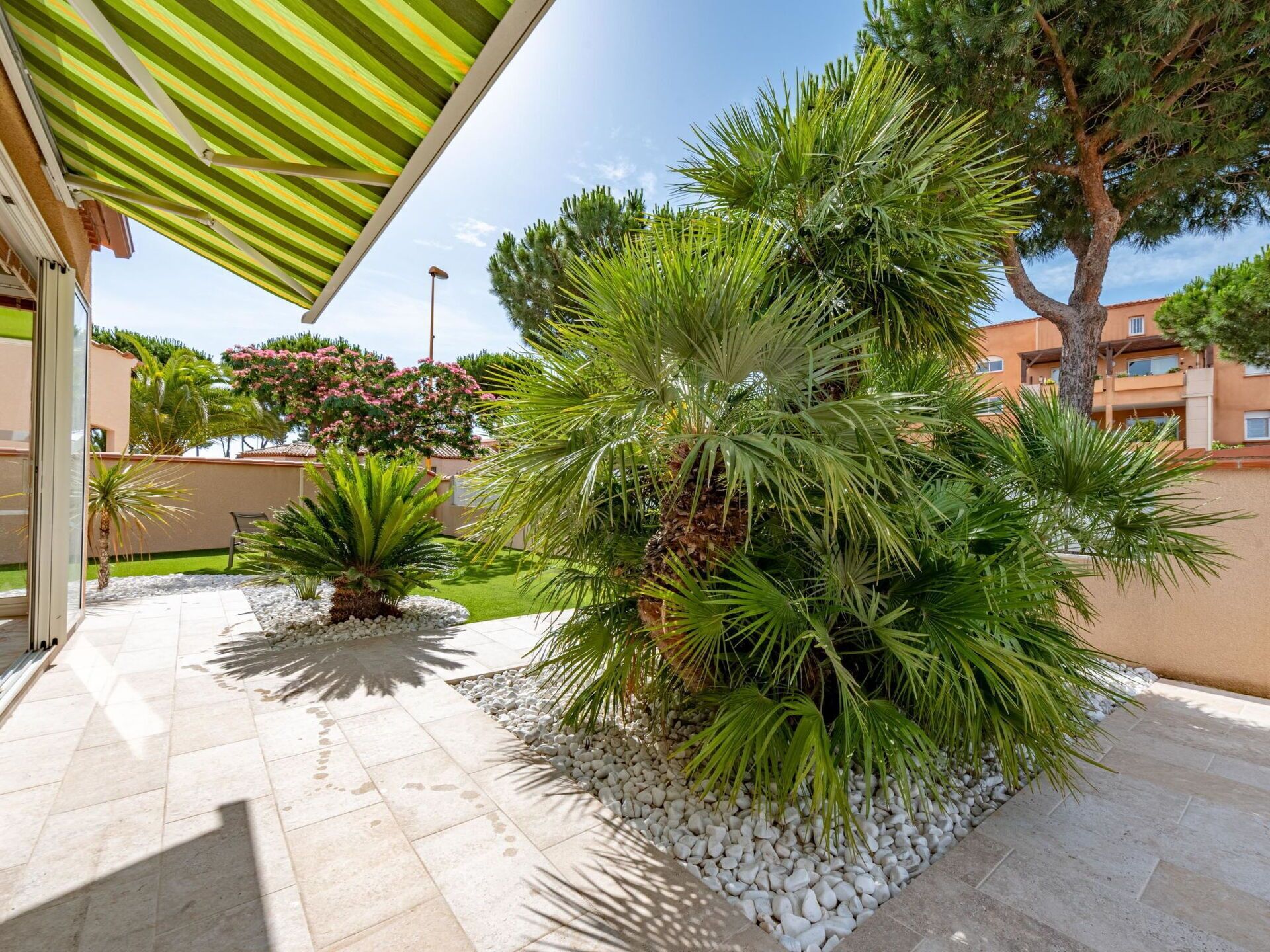 Une cour intérieure agrémentée de palmiers, une terrasse carrelée et un auvent à rayures.