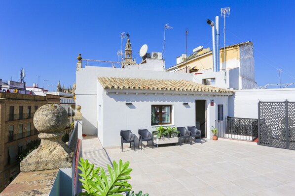 Una terraza en la azotea con zona de estar, barandilla de piedra decorativa y vistas a la ciudad.