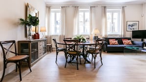 A spacious living room with a dining area, large windows with curtains, a sofa, and a flat-screen TV.