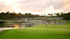 Campo de golf con obstáculo acuático y un jugador preparándose para hacer un putt.