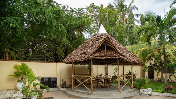 A thatched-roof gazebo with a table and chairs, surrounded by tropical plants and trees. - Stunning 2Bd Apt in Mombasa/Mtwapa- Your Home (Mombasa/Mtwapa)