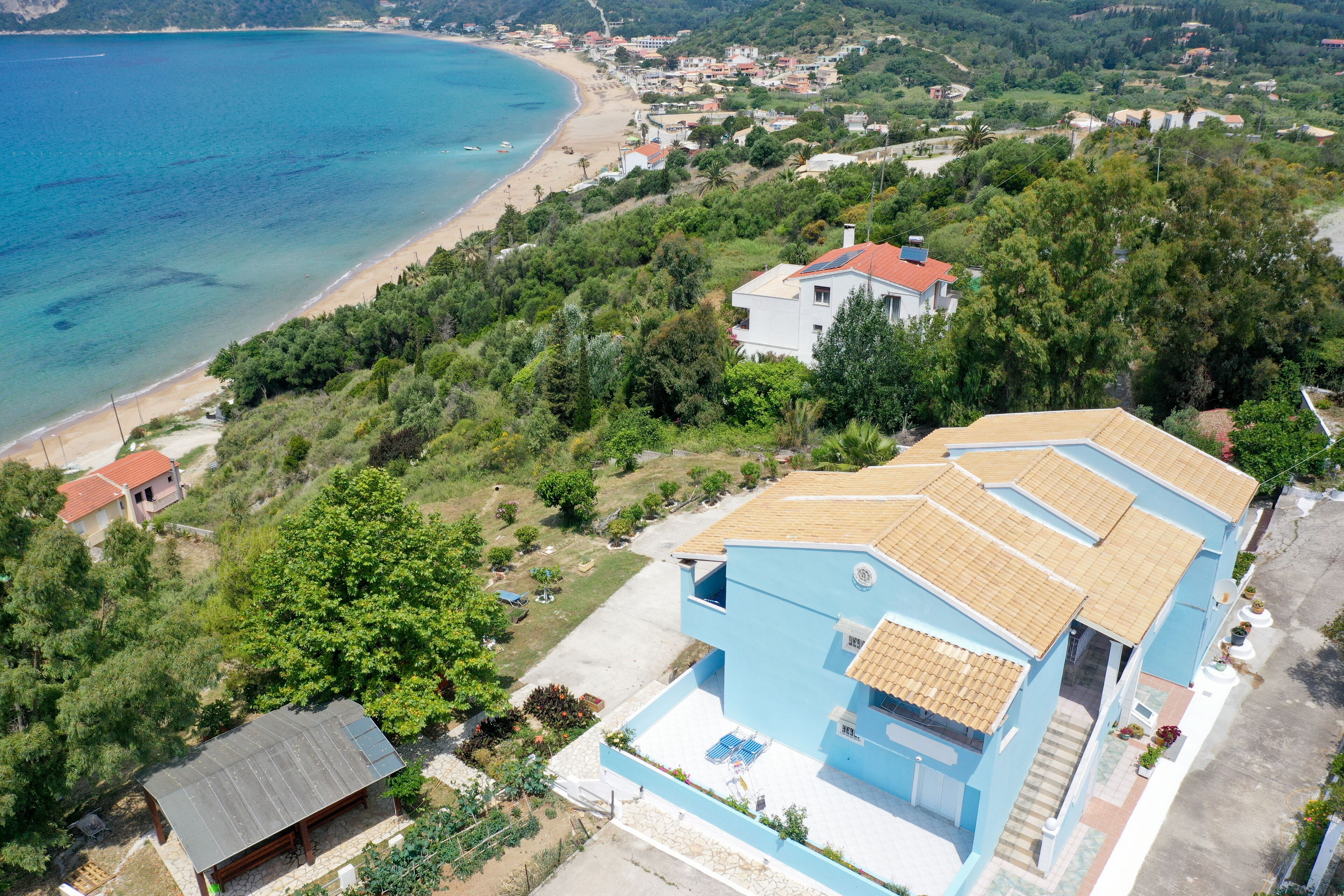 A coastal property with a large blue house, a small adjacent structure, and a beach view.