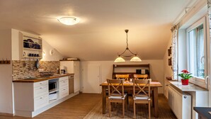 A kitchen with a dining area, wooden chairs, a chandelier, and a window with curtains. - Apartment Brigitte in Garmisch-Partenkirchen with Mountain View (Garmisch-Partenkirchen)