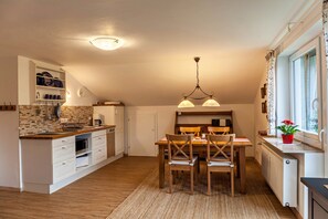 Una cocina con comedor, sillas de madera, una araña y una ventana con cortinas.