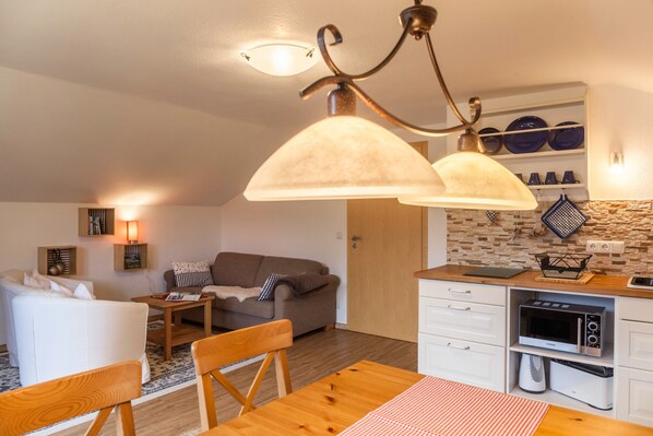 Un espacio habitable compacto con kitchenette, comedor y zona de estar con sofá y mesa.