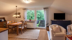 A cozy living room with a dining area, a television, and a balcony with a view of greenery. - Apartment Brigitte in Garmisch-Partenkirchen with Mountain View (Garmisch-Partenkirchen)