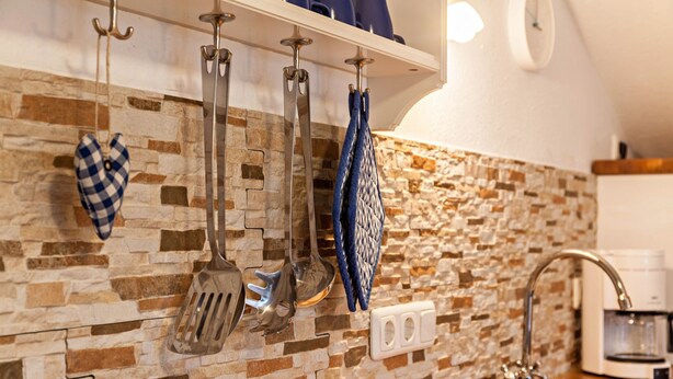A kitchen with stone backsplash, hanging utensils, a coffee maker, and a sink. - Apartment Brigitte in Garmisch-Partenkirchen with Mountain View (Garmisch-Partenkirchen)