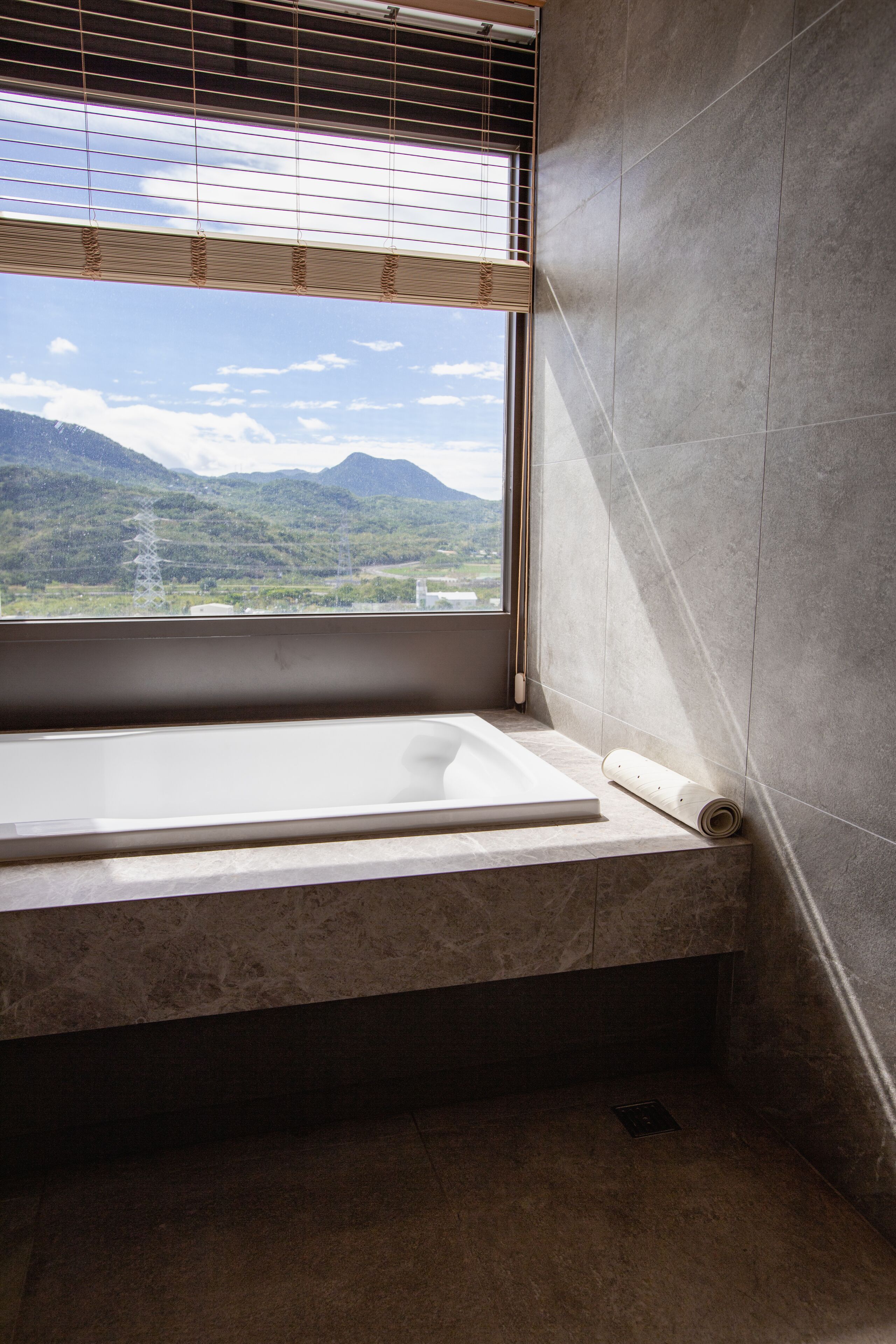 A bathroom with a bathtub, a window with a view of mountains, and a towel on the floor.