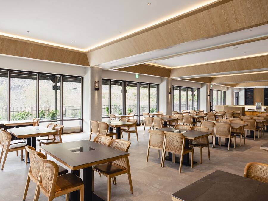 A spacious restaurant with high ceilings, large windows, and a mix of wooden and upholstered chairs.