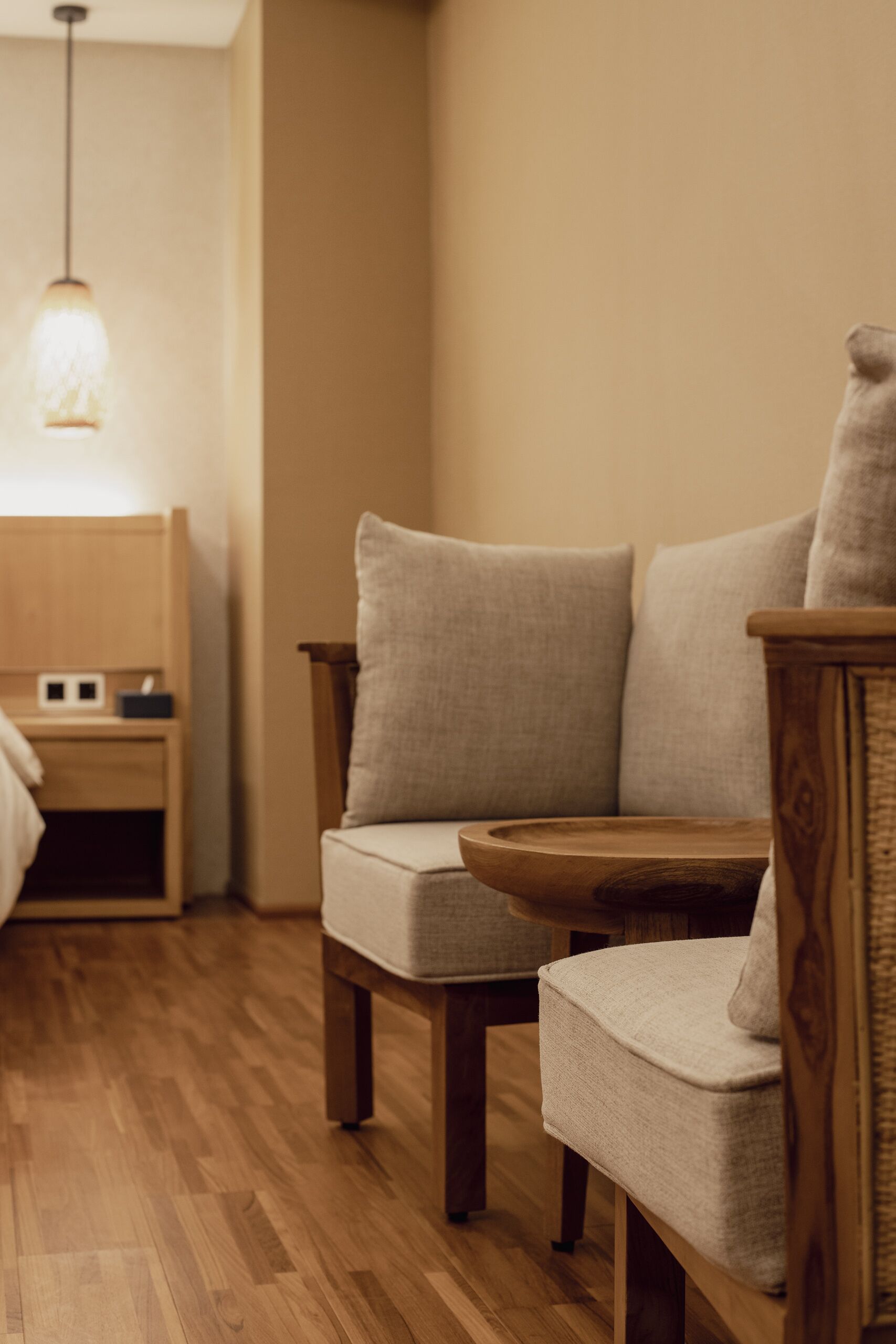 Une pièce chaleureuse avec un plancher en bois, une table de chevet en bois, une lampe et deux fauteuils rembourrés, ainsi qu’une petite table en bois.