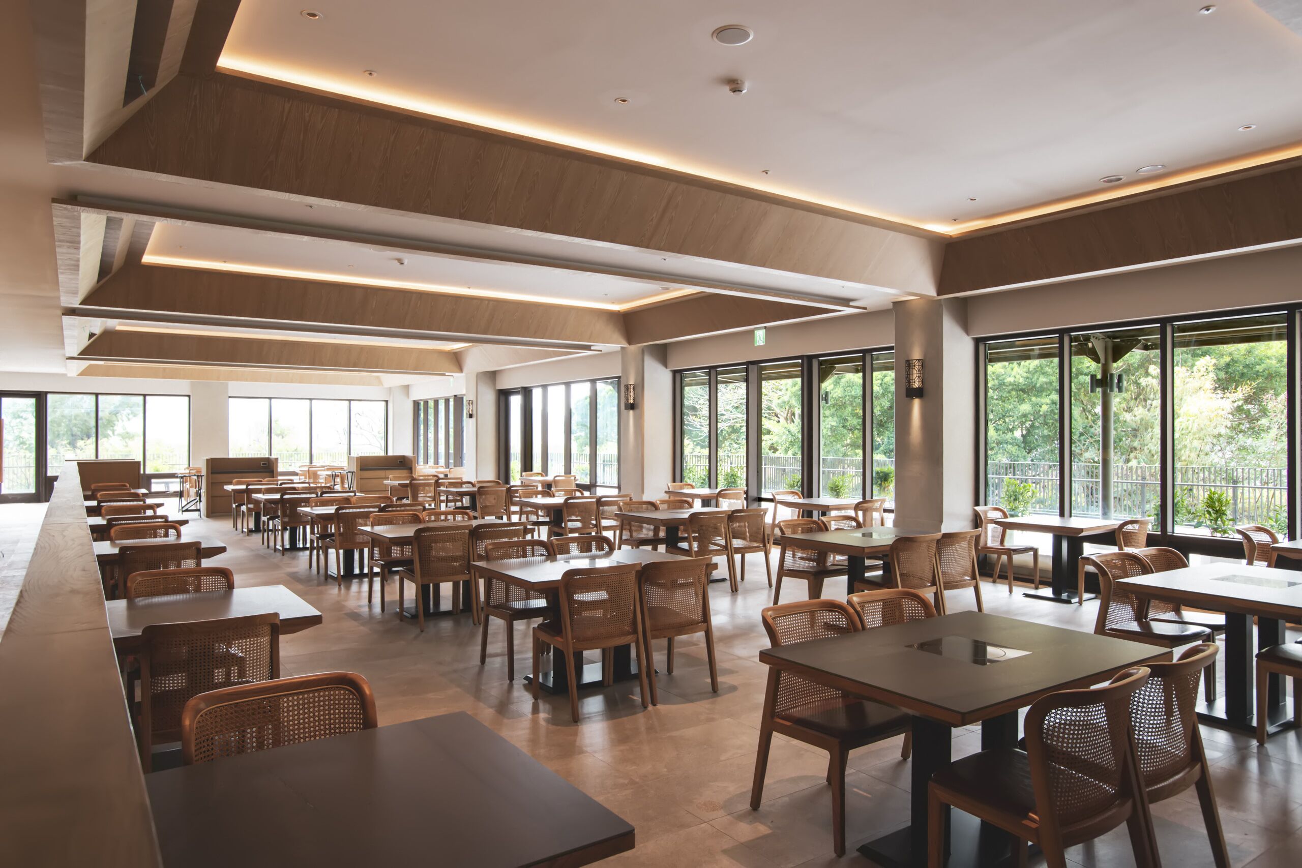 A spacious dining area with multiple tables and chairs, large windows, and a modern ceiling design.