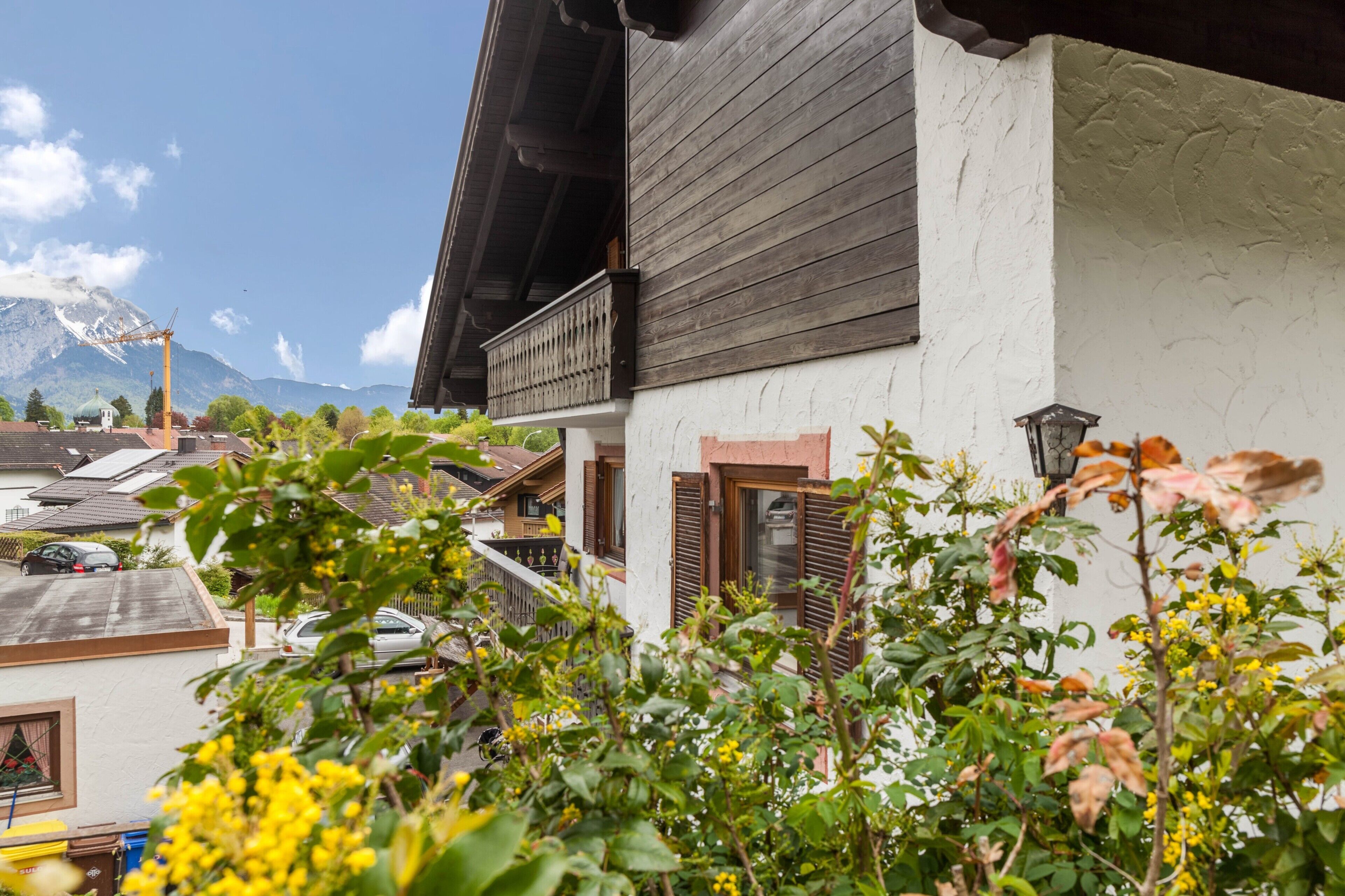 Ein traditionelles Gebäude mit Balkon, einem Berg im Hintergrund und einem Garten im Vordergrund.