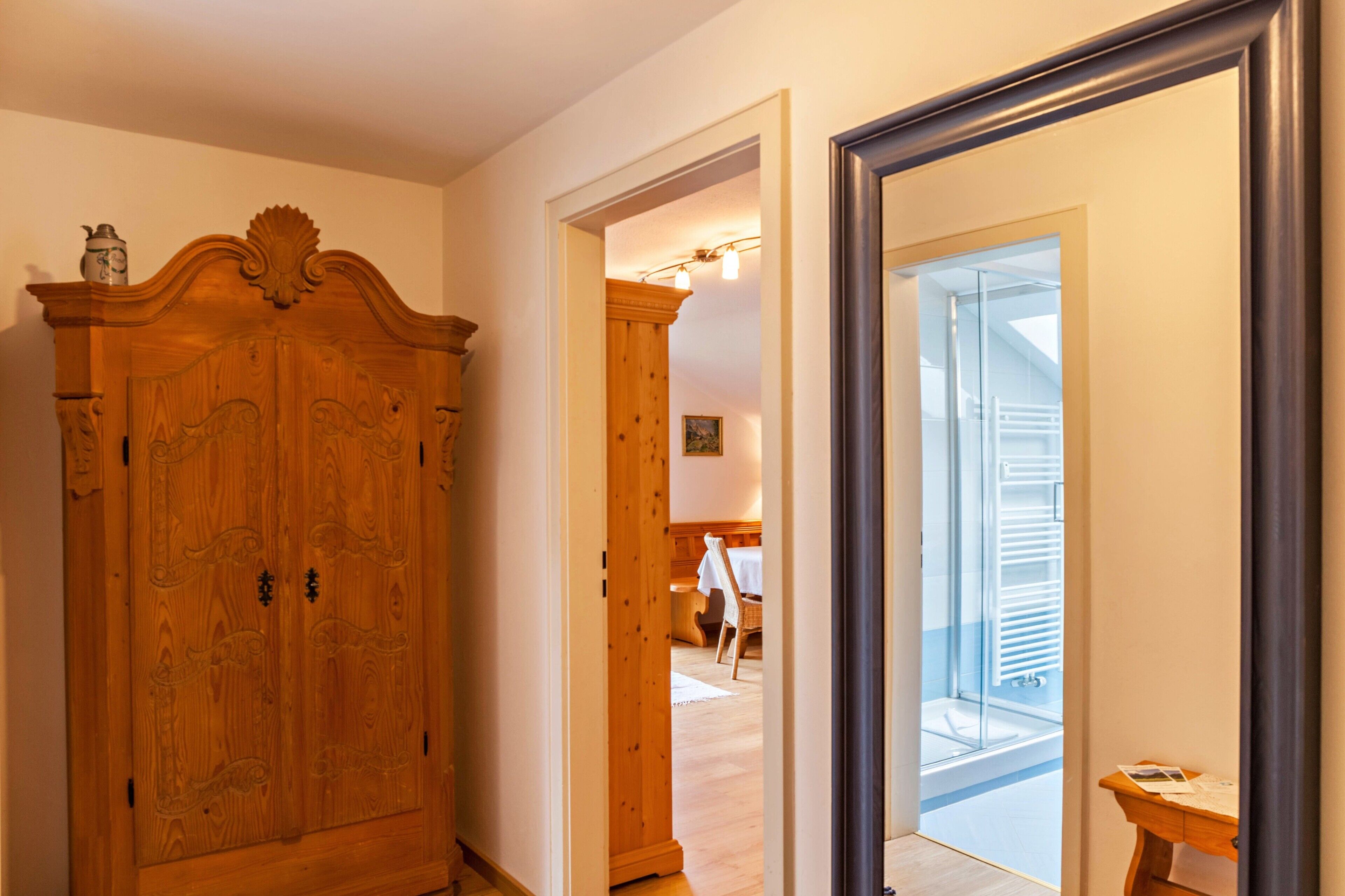 Ein Holzschrank, ein Durchgang zu einem Zimmer mit Bett und Sessel, und ein großer Spiegel.